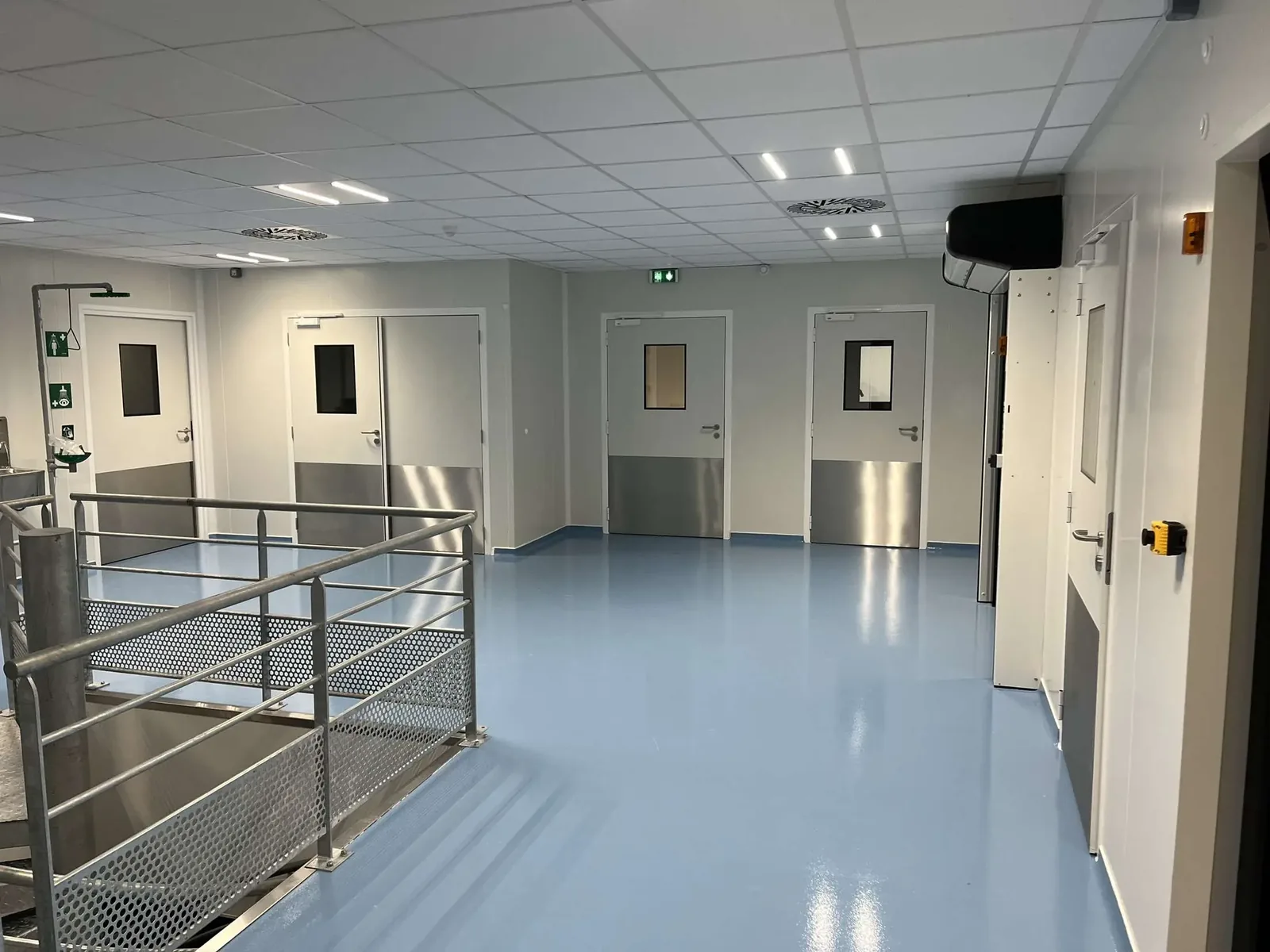 Sas d'une salle grise rénovée avec portes à protection inox et douche de sécurité